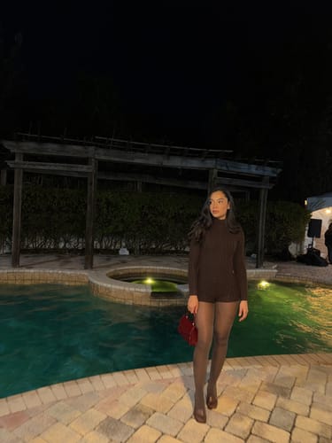 Customer wearing the dark chocolate Cable Knit Turtleneck Romper with tights outdoors at night.