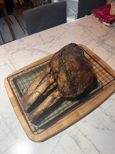 Customer's cooked Tomahawk Prime Rib Roast with three bones resting on a wire rack on a kitchen counter.