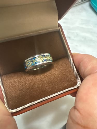 Customer holding open a jewelry box to display the Rustic Stainless Steel Ring, showing its blue inlay and gold 'Jesus' design.