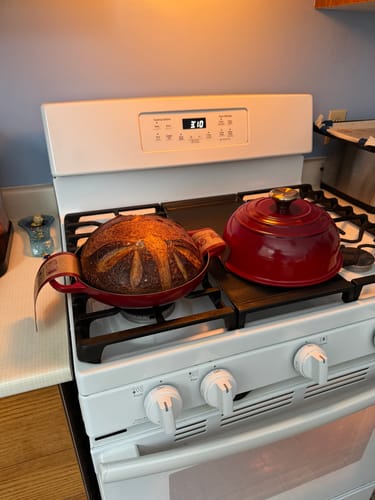 Customer's red Le Creuset Cast Iron Bread Oven on a stove with a freshly baked loaf in the open base.