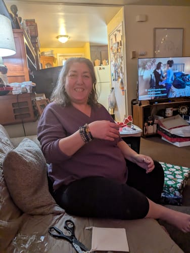 Customer smiling while wearing the multi-wrap Mala Bead Bracelet on her wrist while sitting on a couch.