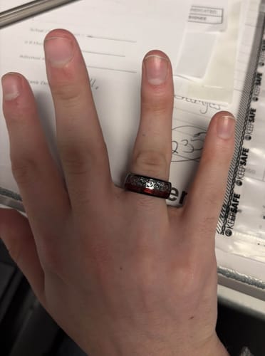 A customer's hand wearing the Ignis ring, showcasing the black band with its red and silver inlay.