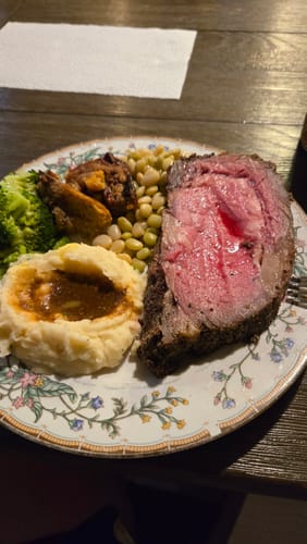 Customer's plated meal with a thick, pink slice of Smoked Prime Rib and side dishes.