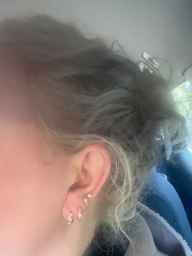 Close-up of a customer's ear with the Solitaire flatback Gold stud in a cartilage piercing, styled with other gold earrings.