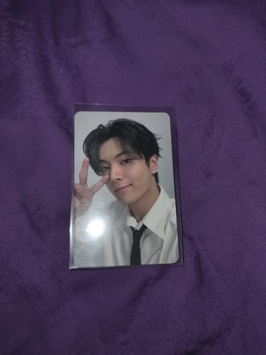 A customer's Enhypen VR photocard showing a person in a white shirt making a peace sign inside a clear sleeve.