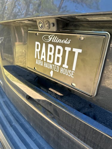Customer's custom Illinois blackout license plate with the text 'RABBIT' and 'AURA HAUNTED HOUSE' on the back of a car.