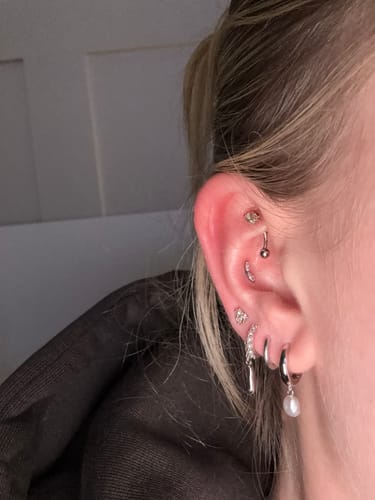 Customer's ear with multiple piercings, showing the Gilded leaf flatback Silver in a flat piercing.