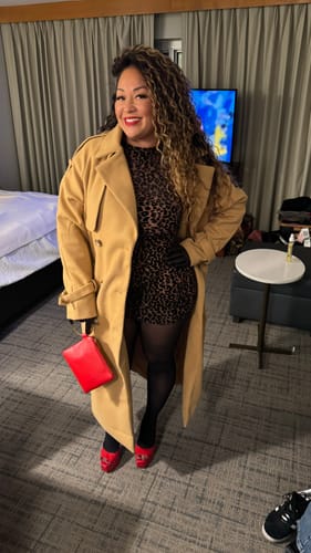 Customer wearing the Burnout Print Mini Dress layered under a long tan coat with a red clutch.