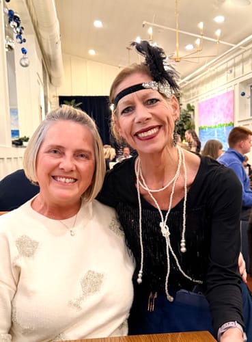 Reviewer wearing the cream Make A Toast Sweater with sparkly glasses design at a party.