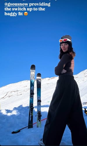 Reviewer standing on a snowy slope, wearing the baggy black snow pants.