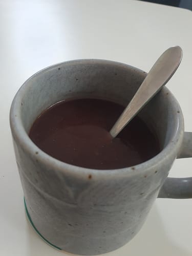 Customer's Mylk Chocolate prepared as hot chocolate in a grey speckled mug with a spoon.