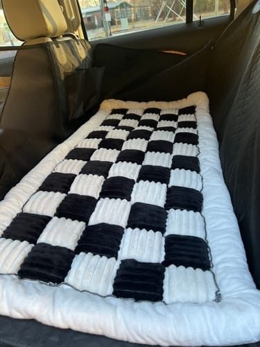 Reviewer's black Car Seat Hammock Cover installed in a vehicle's back seat, with a checkered blanket laid on top.
