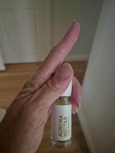 Customer holding the Aurora Nectar roll-on perfume and gesturing number one with their finger.