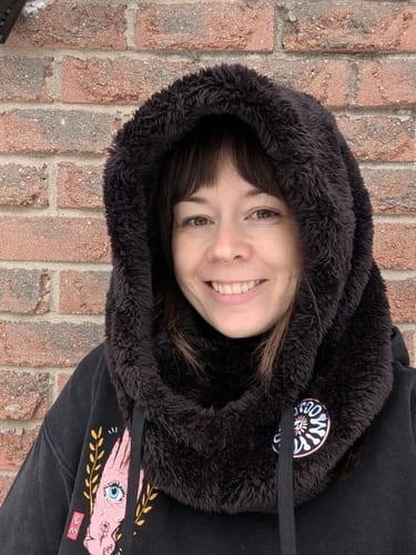 Customer smiling while wearing a cozy, black fleece Fuzzy Hood outdoors.
