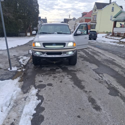 Customer's white truck with bright Carifex LED Headlights and a light bar on, parked on a snowy street.
