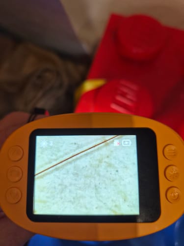 Ein Kunde zeigt das gelbe Edubini Abenteuer-Mikroskop, dessen Bildschirm eine Nahaufnahme eines Haares zeigt.