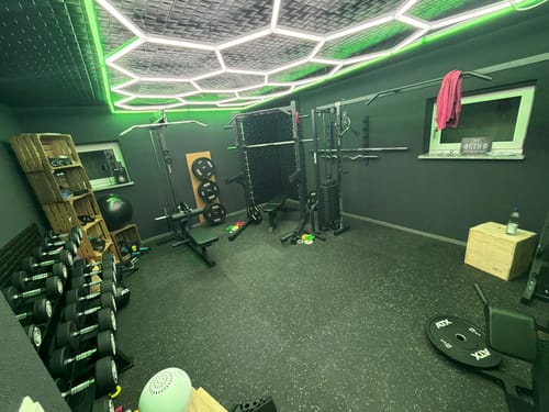 Kunde zeigt den schwarzen Latzug mit Ruder-Station, aufgebaut in einem modernen und gut ausgestatteten Home Gym.