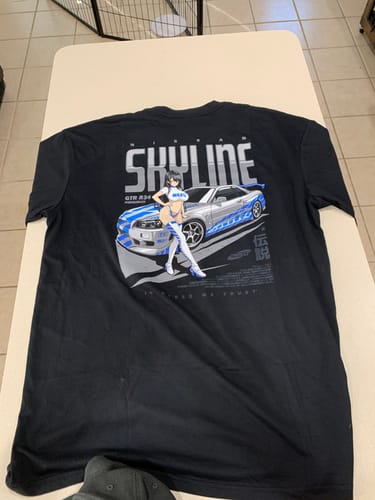 Reviewer's black SKYLINE WAIFU TEE laid flat, showing the large graphic of a car and anime woman on the back.