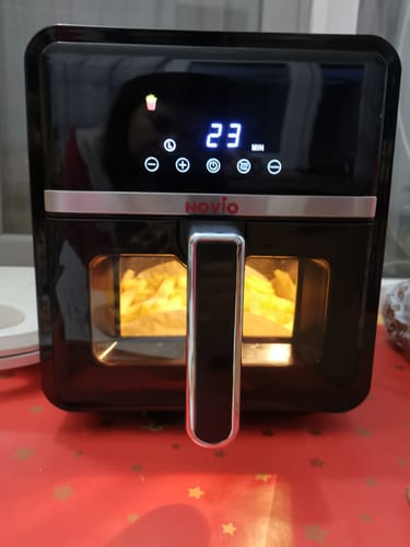 Client arătând friteuza Air Fryer Novio StonePro în timpul funcționării, cu cartofi prăjiți vizibili în coșul iluminat.