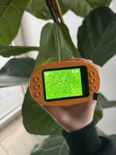 Rezensent hält das orangefarbene Edubini-Mikroskop, dessen Bildschirm die grüne, vergrößerte Struktur eines Blattes zeigt.