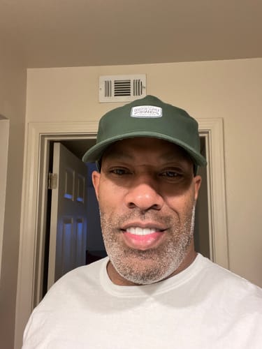 Reviewer smiling while wearing the green Big Relaxed Capp, showing its fit.