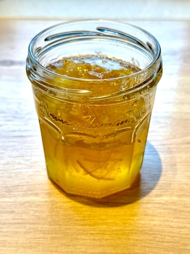 Rezensent zeigt ein Glas selbstgemachter Bergamottenmarmelade auf einem Holztisch.