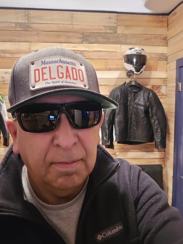 Reviewer wearing the dark gray Massachusetts Plate Hat customized with 'DELGADO', showing the flat bill and green undervisor.