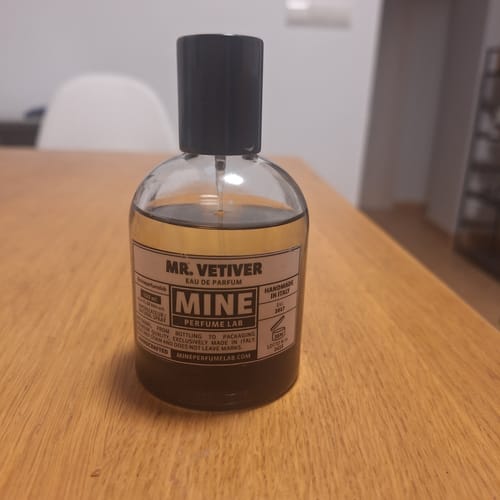 Recensore mostra il flacone di eau de parfum MR. VETIVER su un tavolo di legno.