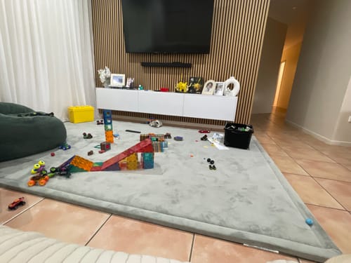 Customer's light grey Mellow Mat in a living room, covered with colorful children's building toys.