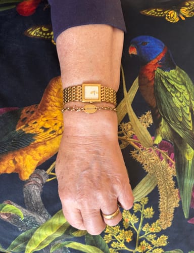 Customer's gold Engravable Chunky Oval Bracelet shown on a wrist, layered with a gold watch.