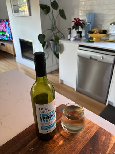 Customer's bottle of Sauvignon Blanc with a poured glass on a wooden board in a kitchen.