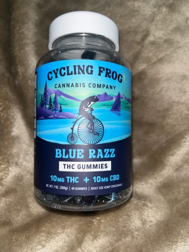 Customer's full bottle of Cycling Frog Blue Razz THC + CBD Gummies on a soft surface.