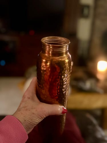 Customer holding the shiny, hand-hammered Pure Copper Water Bottle in a softly lit room.