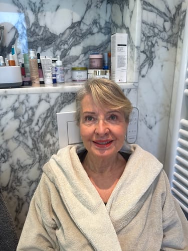 Customer smiling in a bathrobe, showing off their smoother skin in a marble bathroom setting.