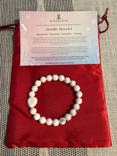 Customer's howlite bracelet with white beads and a heart charm, on its red storage pouch.