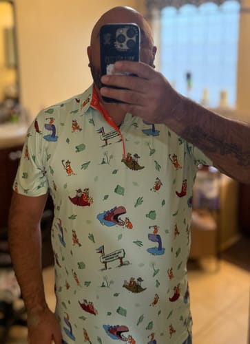 Reviewer wearing The Flintstones polo shirt, showing off the clear graphics and fit in a mirror selfie.