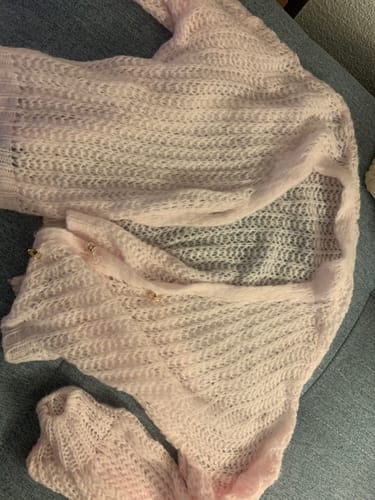 Rezensent zeigt den hellrosa Feiner Lochstrick Cardigan, der auf einer dunklen Oberfläche ausgebreitet ist.