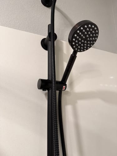 Reviewer's black all-metal Handheld Shower Head mounted on a slide bar in a shower.