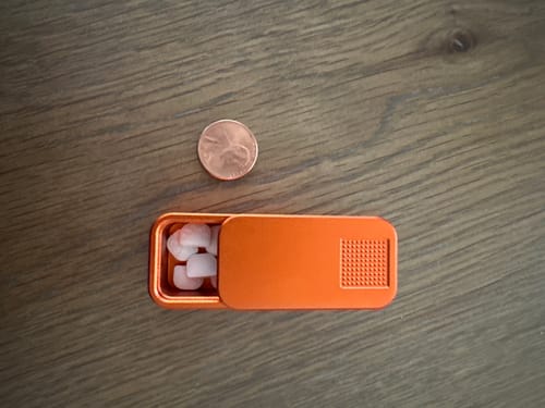 Reviewer's small orange pill case, shown open with a penny next to it for size comparison.