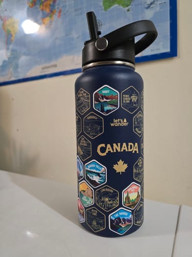 Reviewer's navy blue Canada Bottle with several colorful destination stickers applied, sitting on a white surface.