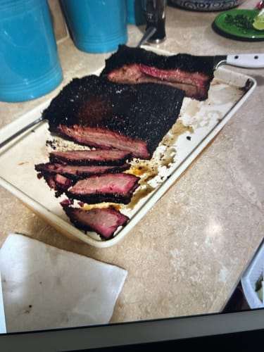 Customer's cooked USDA Prime Brisket with a dark bark, sliced on a baking sheet to reveal a pink smoke ring.