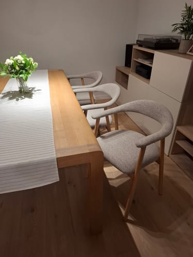 Klantfoto van drie greige Nordic eetkamerstoelen aan een eikenhouten eettafel in een woonkamer.