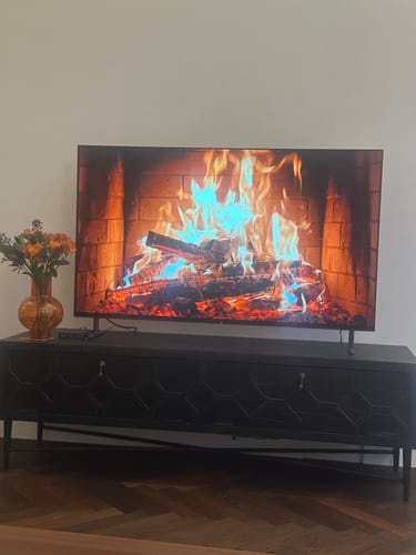 Recensents donkere WOOOD Bequest Tv-meubel in een woonkamer met een televisie erop.