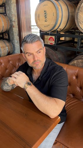 Reviewer wearing the rose gold Lucky Fours® Oceanus watch while sitting at a wooden table.