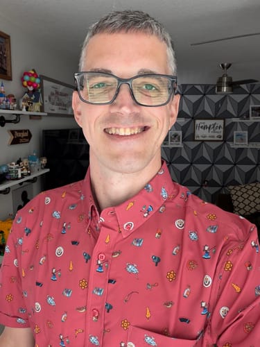 A customer smiling while wearing the red 'Road Trip Trinkets' KUNUFLEX Short Sleeve Shirt.