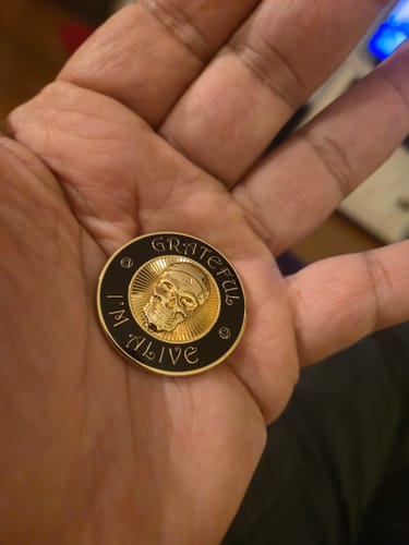 Customer holding the black and gold 'Grateful I'm Alive' recovery medallion in their hand.