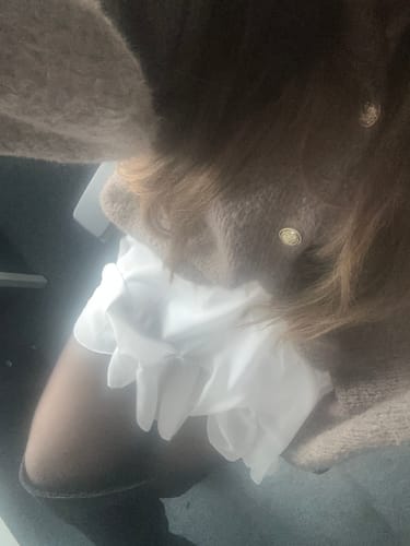 Eine Kundin trägt den Oversized-Cardigan „CozyGlam“ aus Grobstrick über dem weißen Rock „Summer“.