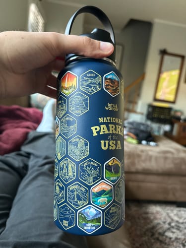 Reviewer holding the blue National Parks Water Bottle, showing the engraved design with some colorful stickers applied.