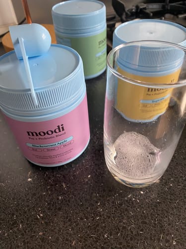 Customer's collection of moodi Pre + Probiotic tubs in various flavors on a counter next to a glass with a prepared drink.