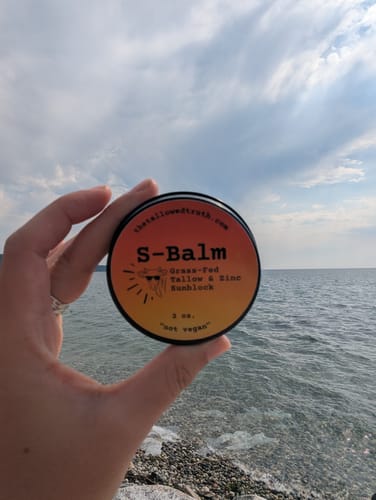 Customer holding a round tin of S-Balm sunblock with a large body of water in the background.